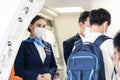 Asian flight attendants wearing face mask greeting passengers walking and coming on board in airplane during the Covid pandemic to Royalty Free Stock Photo