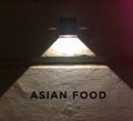 Asian food restaurant facade sign in night. Black text letters on stone wall lighted up with a small street lamp. Small