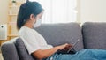 Asian freelance business woman wearing protective mask using tablet working in living room from home. Royalty Free Stock Photo