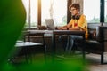 Asian freelance man rewriting content in social network via laptop computer while resting in modern coffee shop, Online work ideas