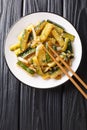 Asian fried zucchini with onions, parsley and sesame seeds in soy sauce close-up in a plate. vertical top view