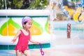 Asian funny girl running through the splash of the fountain courtyard. Happy child dancing with water in summer time.