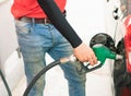 Asian gas station worker man catching green fuel nozzle into one hand while filling high energy power fuel into black auto car