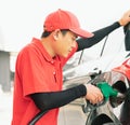 Asian gas station worker man holding green fuel nozzle into one hand and filling high energy power fuel into black auto car tank Royalty Free Stock Photo