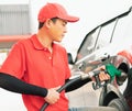 Asian gas station worker man holding green fuel nozzle with two hands and filling high energy power fuel into black auto car tank Royalty Free Stock Photo