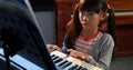 An Asian girl with black hair plays the piano, concentrating on the music sheets Royalty Free Stock Photo