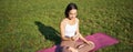 Asian girl follows yoga training app, looking at smartphone, meditating and doing exercises on fresh air in park
