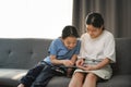 Asian girl and her sister using tablet together while siting on sofa in living room. Royalty Free Stock Photo