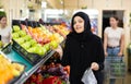 Asian girl in hijab buys ripe apples in supermarket