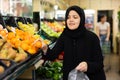 Asian girl in hijab buys ripe tangerines in supermarket