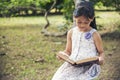 Asian Girl holding book reading at green park in natural garden. Young todler girl relaxation read open book self study. Happy