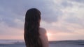 asian girl letting hair down on ocean shore at sunset. Shy and pretty Korean woman undoing hair and turning around