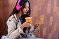 Asian girl listening to music while working, cheerful asian woman drinking coffee outdoors using modern smartphone device Royalty Free Stock Photo