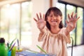 Asian Girl Painting Picture On Table At Home Showing Messy Hands To Camera