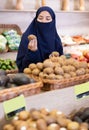 Asian girl in paranja choosing kiwi in grocery