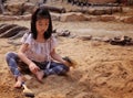 An Asian girl playing in a sandbox with a modeled dinosaur fossil