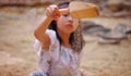 An Asian girl playing in a sandbox, sprinkling sand from a small shovel
