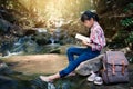 Asian girl reading a book sitting on the rock near waterfall in forest background Royalty Free Stock Photo