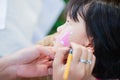 Asian girl sitting for painting face during Easter. An adult`s hand is drawing a rabbit cartoon on a cute child face. Royalty Free Stock Photo