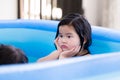 Asian girl is sitting in rubber pool playing at house. Kid rest one\'s chin on one\'s hands.