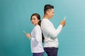 Asian girl and smile guy standing back to back, using mobile phones over blue background Royalty Free Stock Photo