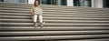 Asian girl student sits on stairs near campus, types on laptop, does her homework outdoors