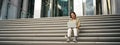 Asian girl student sits on stairs near campus, types on laptop, does her homework outdoors