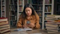 Asian girl student sitting in library write doing homework frustrated young woman getting notification on mobile phone