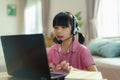 Asian girl student video conference e-learning with teacher and classmates on computer in living room at home. Homeschooling and Royalty Free Stock Photo