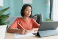 Asian girl is studying online via the internet on tablet and doing homework while sitting in the living room at home morning. Conc Royalty Free Stock Photo