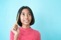 Asian girl thinking and smiling on background blue isolated, Asia child happy holding a pencil while looking Royalty Free Stock Photo