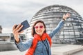 Asian girl travel blogger takes a selfie against the backdrop of the famous glass dome in the Bundestag building in Berlin