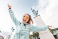 Asian girl traveler funny posing on the background of the famous Statue of Liberty. The concept of tourism and immigration