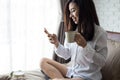 asian girl using smartphone send Message , woman holds cup of coffee in hands on her bed In the white bedroom by the window Royalty Free Stock Photo