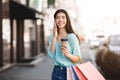 Asian girl walking with shopping bags, drinking coffee and talking on cellphone Royalty Free Stock Photo