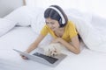 An Asian girl watching a movie, listening to music on her laptop, in bed with a maltese Royalty Free Stock Photo