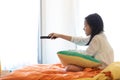 Asian girl watching TV lying on bed with remote control in hand Royalty Free Stock Photo