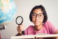 Asian girl wearing glasses is smiling and using a magnifying glass in the classroom, Educational concept Royalty Free Stock Photo
