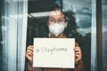 Asian girl wearing glasses, wearing a mask, holding paper labeled stayhome, is bored of having to detain and treat the illness at