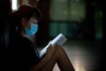 Asian girl wearing a mask sits and reads a book with stress. Concept of learning problems during state quarantine