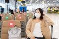 Asian girl wearing mask sitting at international airport while waiting for check in counter open. Social distance in public place