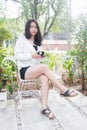 An Asian girl in white coat sitting and holding a black cup of coffe in her hand on the white bench under the morning light. Royalty Free Stock Photo