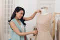An Asian girl is working in the workshop studio. She makes fitting on the dress on the mannequin