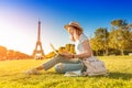 Asian girl works on a laptop sitting on the grass on the Champ de Mars in Paris overlooking the Eiffel tower at sunset. Concept