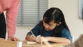 Asian girl writing or taking a note while teacher checking classwork. Pedagogy.