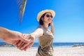 Asian girlfriend wear hat leading man hand to travel on sea beach Royalty Free Stock Photo