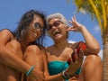 Asian girlfriends in bikini enjoying Summer holidays at tropical beach resort swimming pool having fun using mobile phone together