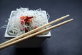 Asian glass funchose noodles and bamboo sticks on a white square plate on a black slate background with copy space. oriental asian