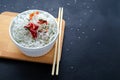 Asian glass fungoza rice noodles and bamboo sticks on a wooden board in a white round bowl with sesame seeds on a black