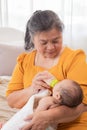 Asian grandmother feeding newborn baby in bedroom. Senior women taking care adorable infant at home. mother enjoying feeding Royalty Free Stock Photo